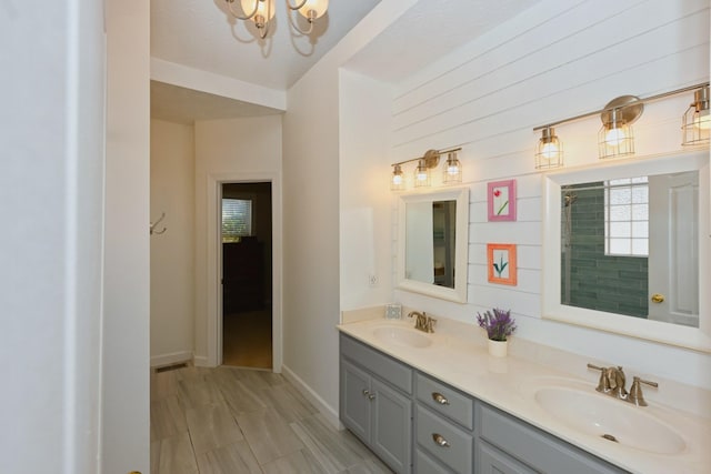 full bath with double vanity, a notable chandelier, baseboards, and a sink