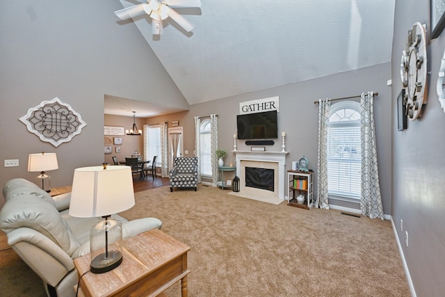 living room featuring high vaulted ceiling, ceiling fan with notable chandelier, a fireplace, carpet flooring, and baseboards