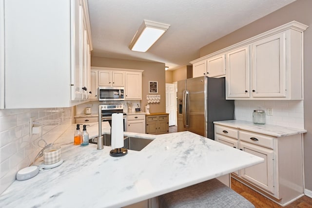 kitchen with tasteful backsplash, light stone counters, a peninsula, stainless steel appliances, and a sink