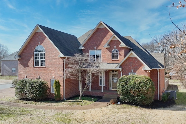 traditional-style house featuring covered porch, roof with shingles, central AC unit, and brick siding