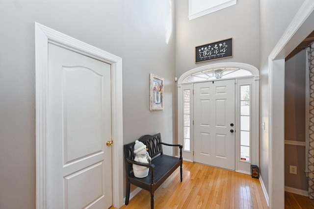 entrance foyer with baseboards, light wood-style flooring, and a towering ceiling