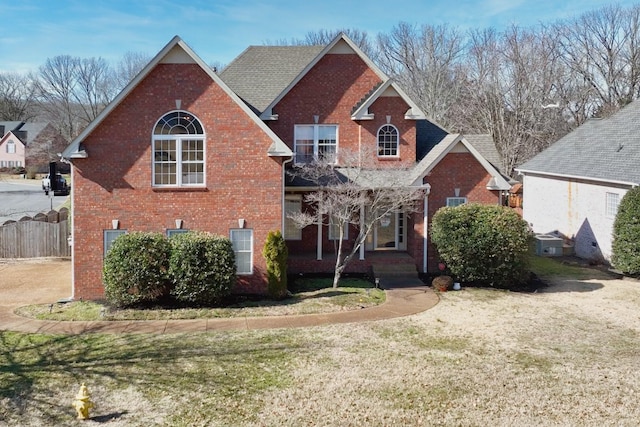 traditional-style house featuring brick siding, a front lawn, and fence