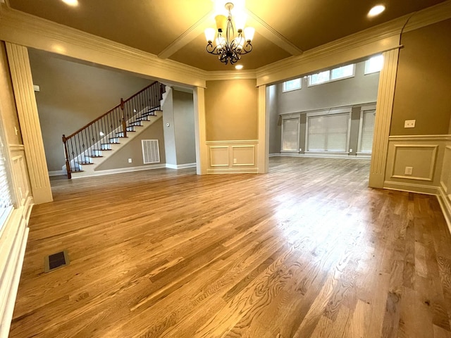 unfurnished living room with visible vents, a decorative wall, a notable chandelier, and stairs