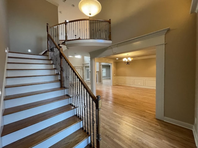 stairway featuring ornamental molding, a decorative wall, a high ceiling, and wood finished floors