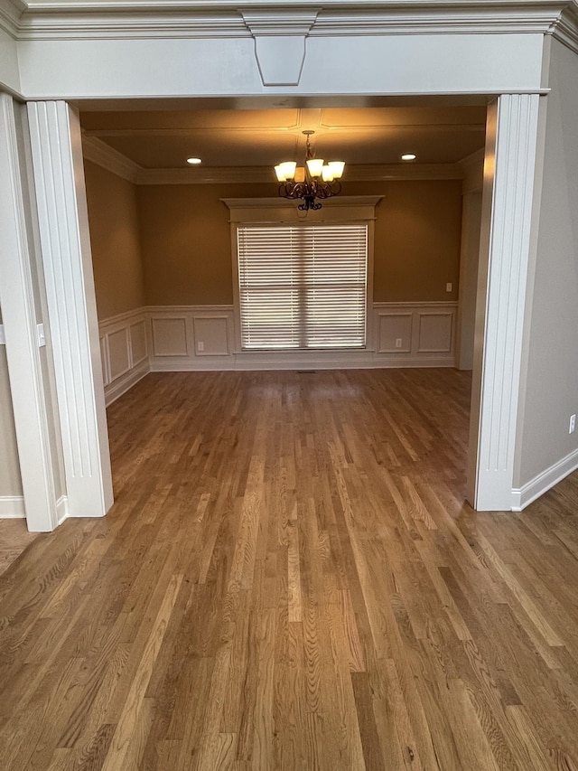 interior space featuring a wainscoted wall, a notable chandelier, a decorative wall, ornamental molding, and wood finished floors