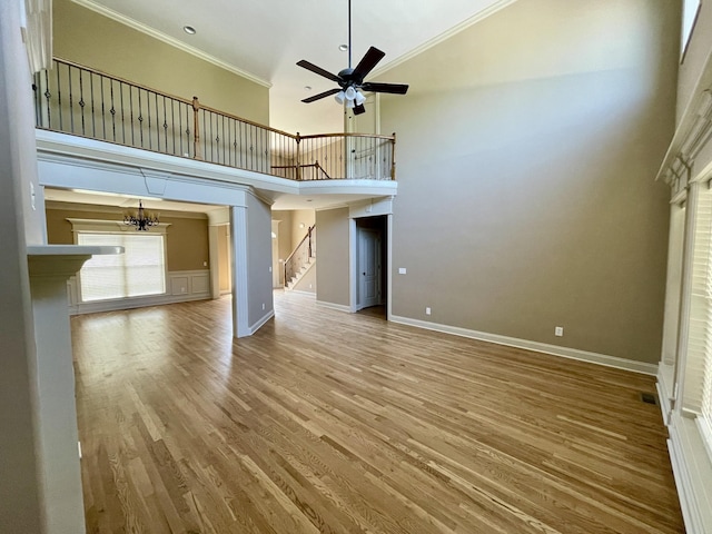 unfurnished living room featuring ceiling fan with notable chandelier, wood finished floors, baseboards, stairway, and crown molding