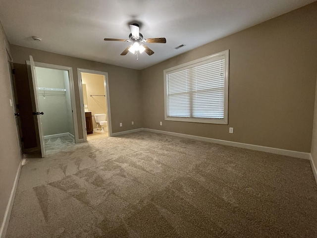 unfurnished bedroom featuring light carpet, baseboards, visible vents, connected bathroom, and a walk in closet