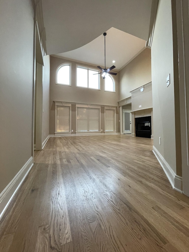 unfurnished living room with a fireplace, a high ceiling, a ceiling fan, wood finished floors, and baseboards