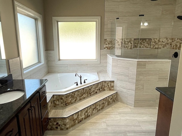 bathroom featuring a tub with jets, a walk in shower, and vanity