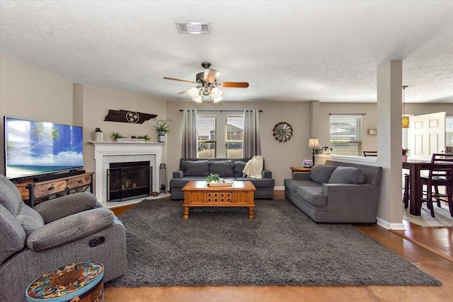 living room with a textured ceiling, visible vents, a wealth of natural light, and a glass covered fireplace