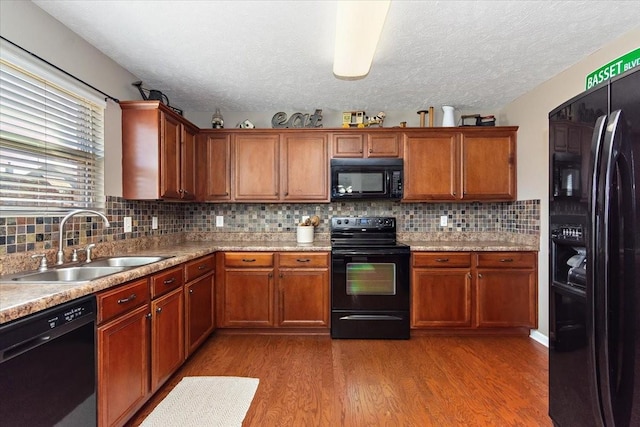 kitchen with light countertops, a sink, black appliances, and wood finished floors