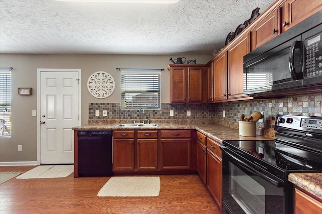 kitchen with brown cabinetry, light wood-style floors, a sink, black appliances, and backsplash