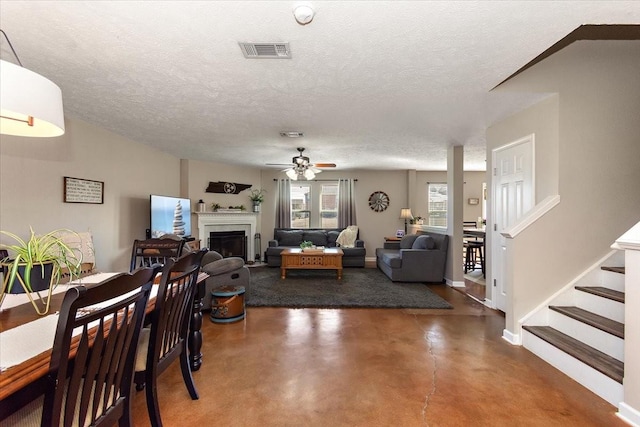 living area featuring visible vents, stairs, a textured ceiling, concrete flooring, and a fireplace