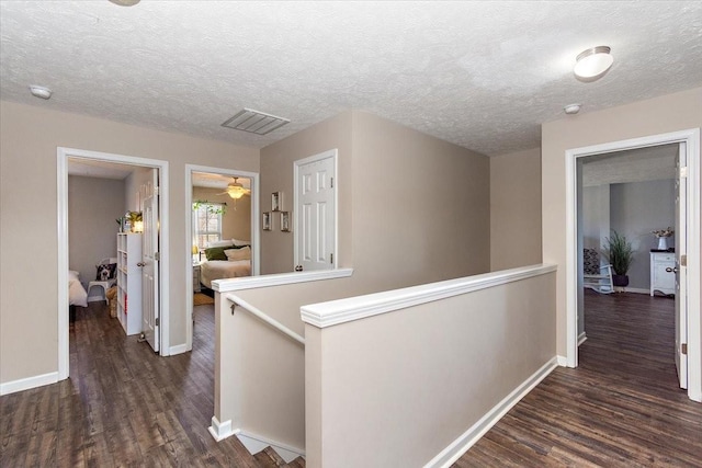 hall featuring visible vents, baseboards, dark wood finished floors, and an upstairs landing