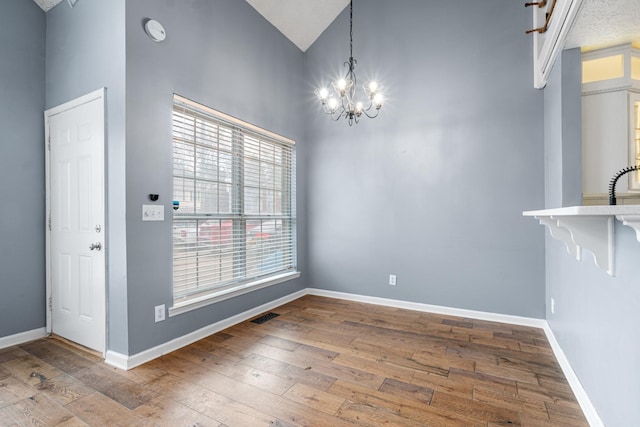 unfurnished dining area featuring baseboards, visible vents, hardwood / wood-style floors, and an inviting chandelier