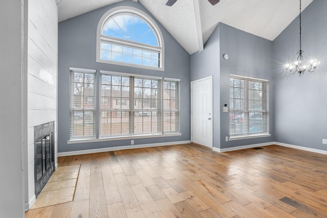 unfurnished living room featuring high vaulted ceiling, ceiling fan with notable chandelier, a fireplace, wood finished floors, and baseboards