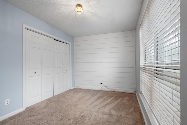 unfurnished bedroom with a textured ceiling, carpet floors, a closet, and wooden walls