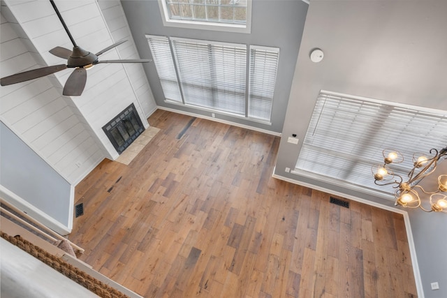 unfurnished living room with baseboards, visible vents, a fireplace with flush hearth, wood finished floors, and ceiling fan with notable chandelier