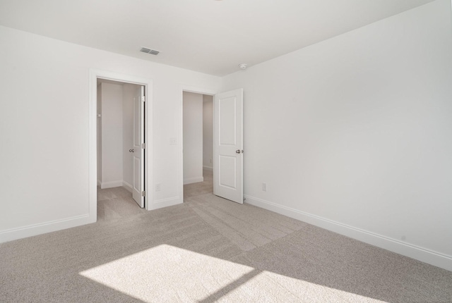 unfurnished bedroom featuring baseboards, a walk in closet, visible vents, and light colored carpet