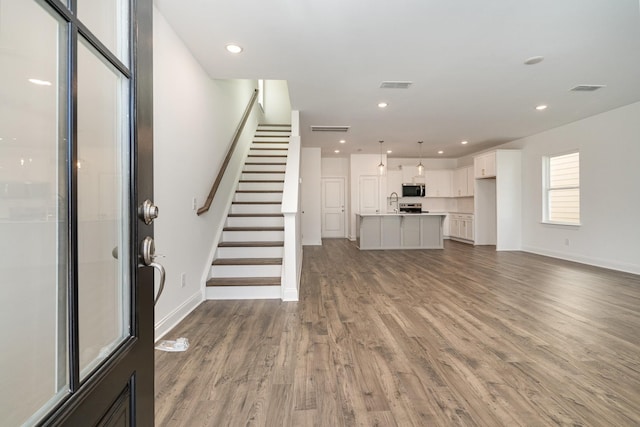 unfurnished living room featuring stairs, visible vents, wood finished floors, and recessed lighting