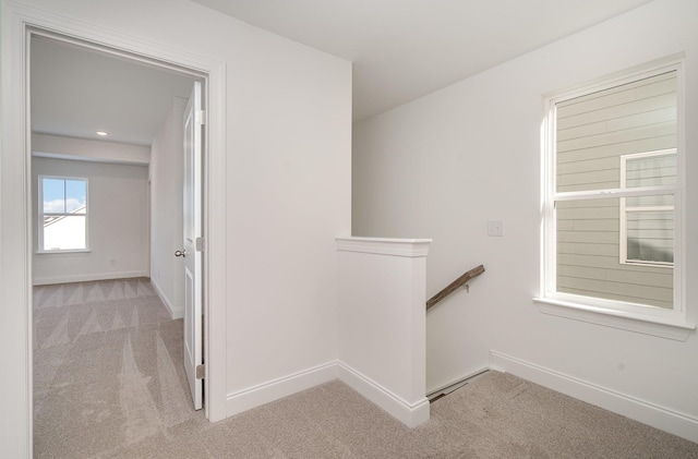 corridor featuring light carpet, baseboards, and an upstairs landing