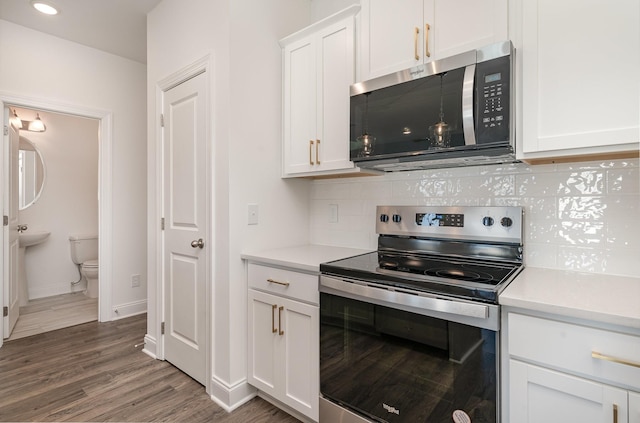 kitchen with stainless steel appliances, tasteful backsplash, light countertops, white cabinets, and wood finished floors