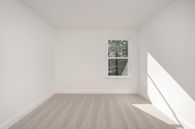 spare room with baseboards and light colored carpet