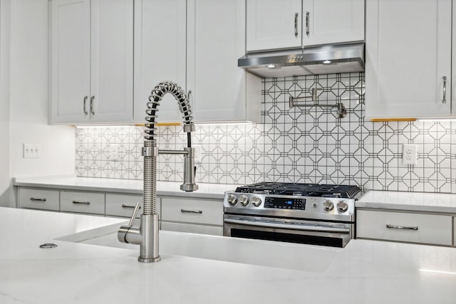 kitchen featuring stainless steel gas range oven, ventilation hood, backsplash, and white cabinets