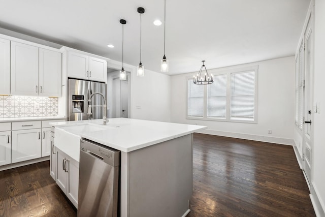 kitchen with stainless steel appliances, dark wood-type flooring, light countertops, backsplash, and decorative light fixtures