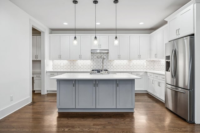 kitchen featuring dark wood finished floors, stainless steel refrigerator with ice dispenser, light countertops, decorative backsplash, and under cabinet range hood