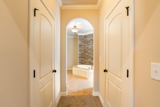 hall with ornamental molding, arched walkways, light colored carpet, and baseboards