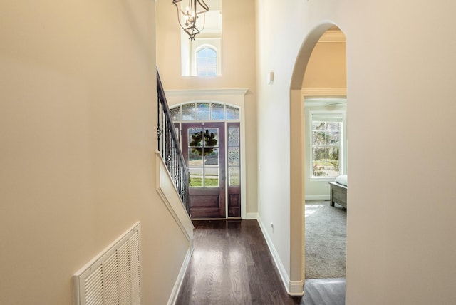 foyer entrance featuring arched walkways, dark wood-type flooring, a towering ceiling, visible vents, and baseboards