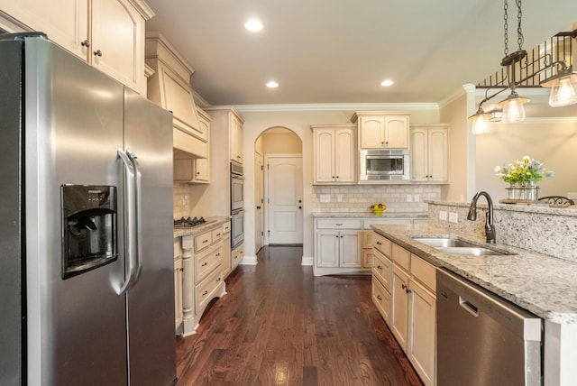 kitchen with arched walkways, dark wood-style floors, appliances with stainless steel finishes, cream cabinets, and a sink