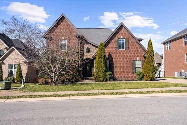 traditional-style home featuring brick siding, stone siding, roof with shingles, central air condition unit, and a front yard