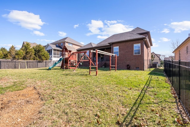 back of property with a playground, a fenced backyard, brick siding, crawl space, and a lawn