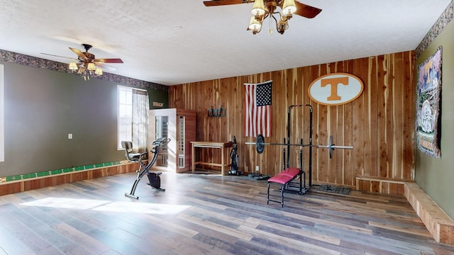 exercise room featuring a textured ceiling, ceiling fan, wooden walls, and wood finished floors