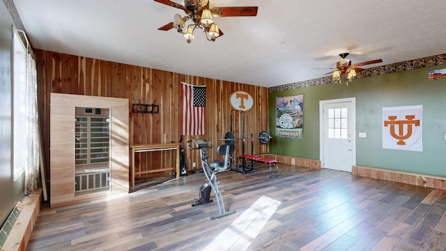 exercise area featuring ceiling fan, wooden walls, and wood finished floors