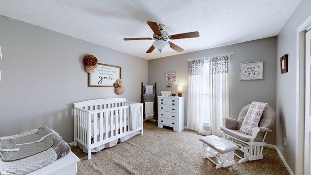 carpeted bedroom featuring a nursery area, baseboards, a ceiling fan, and a textured ceiling