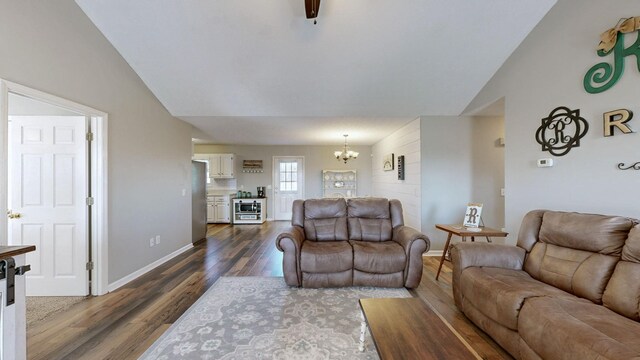 living room featuring dark wood-style floors, lofted ceiling, a chandelier, and baseboards