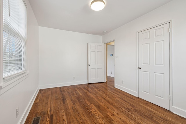 unfurnished bedroom with dark wood-style floors, baseboards, and visible vents