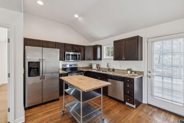 kitchen featuring dark brown cabinetry, wood finished floors, a sink, vaulted ceiling, and appliances with stainless steel finishes