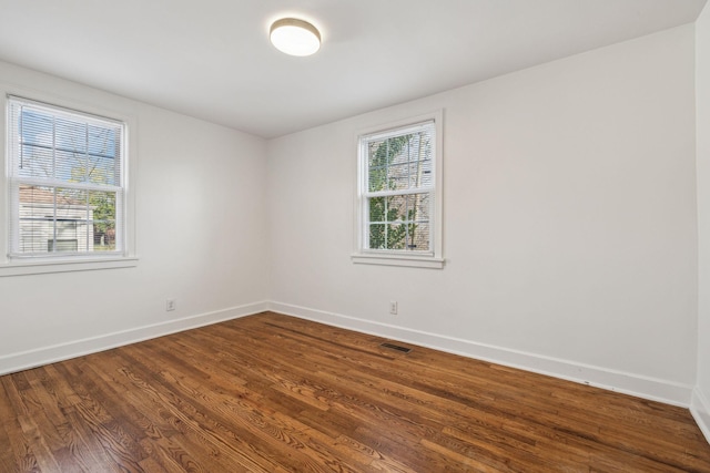 spare room featuring dark wood-style flooring, a healthy amount of sunlight, and baseboards