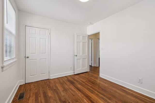 unfurnished bedroom with dark wood-style floors, baseboards, and visible vents