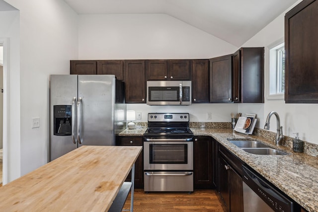 kitchen with lofted ceiling, dark brown cabinetry, stainless steel appliances, butcher block counters, and a sink