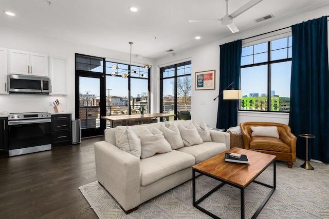 living room with dark wood-type flooring, recessed lighting, visible vents, and ceiling fan with notable chandelier