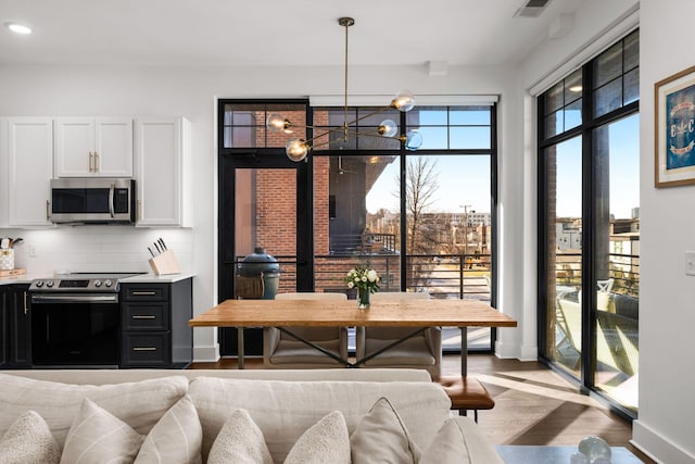 kitchen with light wood finished floors, stainless steel appliances, backsplash, white cabinetry, and baseboards