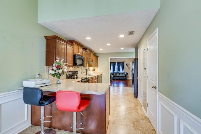 kitchen with visible vents, brown cabinetry, a peninsula, light countertops, and black appliances