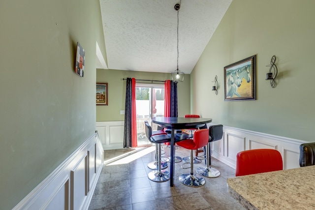 dining space with wainscoting, vaulted ceiling, a textured ceiling, and a decorative wall