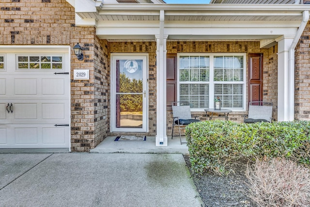 view of exterior entry with covered porch, brick siding, and an attached garage