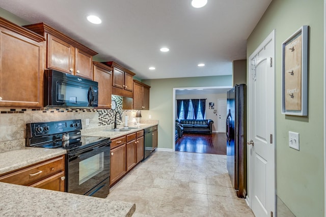 kitchen featuring light countertops, backsplash, brown cabinetry, a sink, and black appliances